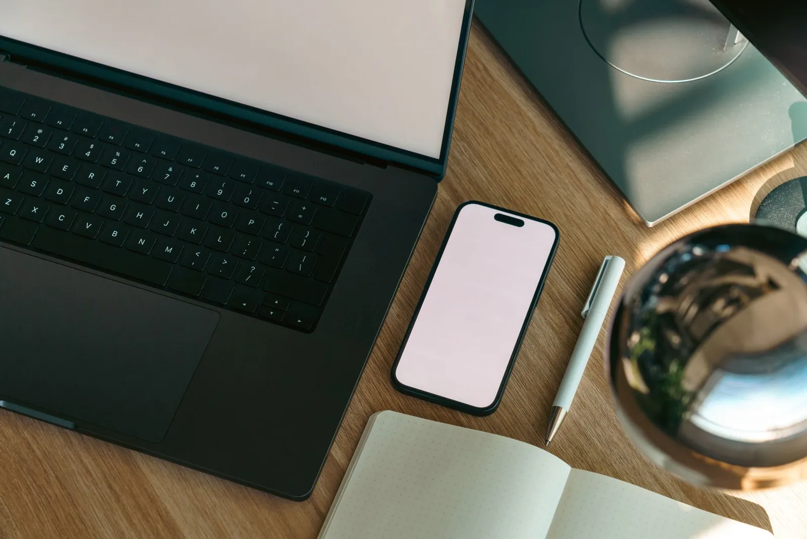 Mesa de madeira com notebook, celular e caderno vistos de cima